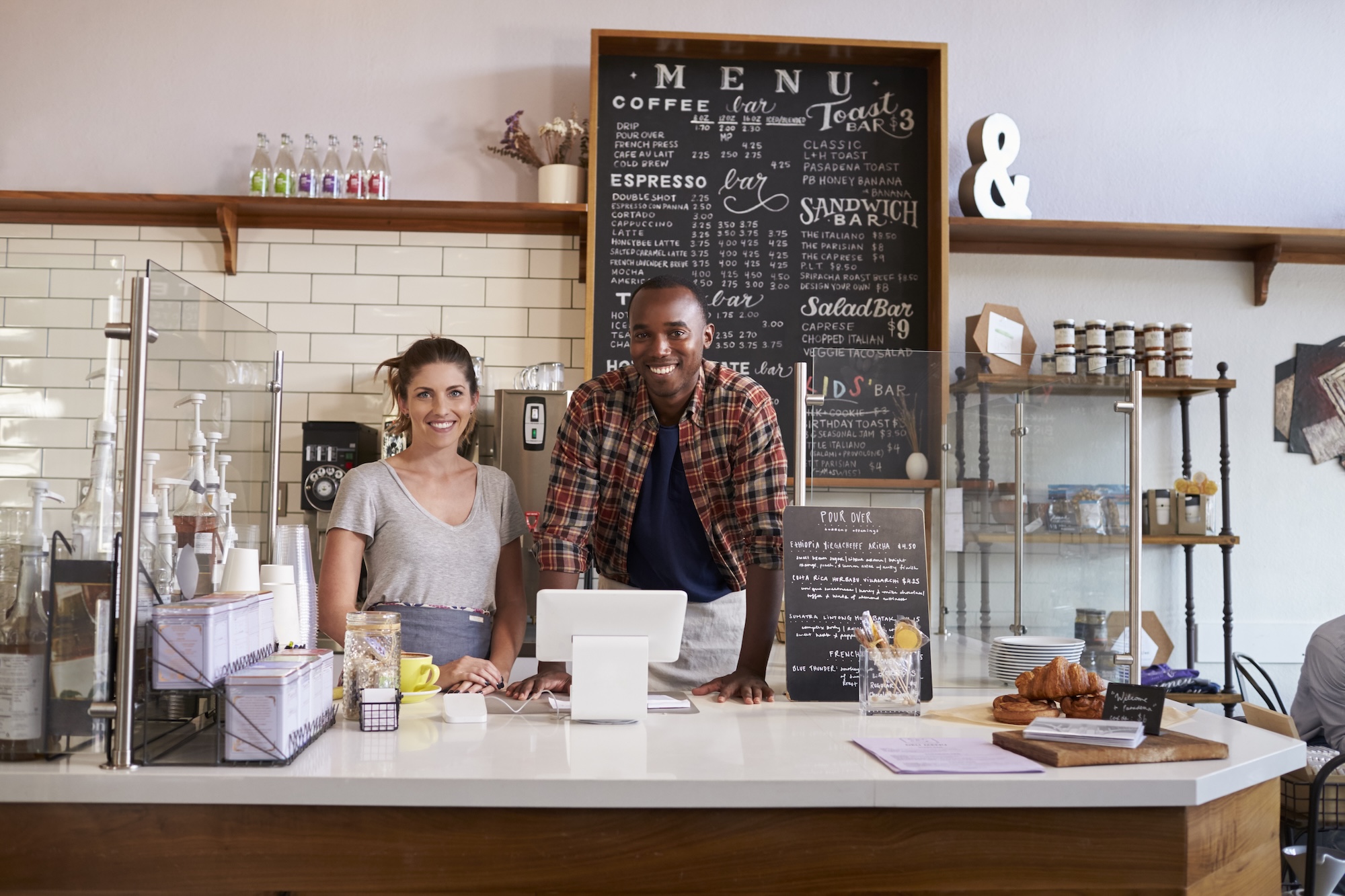 Two local small business owners smiling behind the counter of their coffee shop